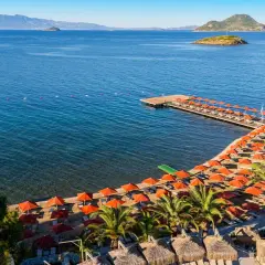 Piękna plaża z rzędem pomarańczowych parasoli i leżaków, drewniany pomost, palmy i turkusowe morze. Idealne miejsce na wakacje, zgodnie z kadikale resort opinie.