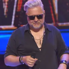 Ira i przyjaciele na scenie. Mężczyzna w okularach przeciwsłonecznych i czarnej koszuli trzyma mikrofon.