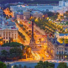 Vista aerea di Barcellona di notte, con la Rambla illuminata, palme e locali notturni che brillano.
