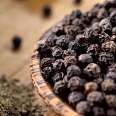 Schwarze Pfefferkörner in einer Holzschale, daneben gemahlener Pfeffer. So wird Pfeffer hergestellt: Ernte, Trocknung und Mahlung.