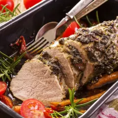 Un délicieux roti de veau aux herbes, servi dans un plat avec des tomates cerises et du romarin.