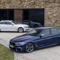 Dwa BMW, jeden granatowy, drugi biały, przed nowoczesnym budynkiem. Czy to xdrive co to za napęd?