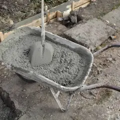 Taczka z betonem i łopatą czeka na wylanie zbrojenia ławy fundamentowej.