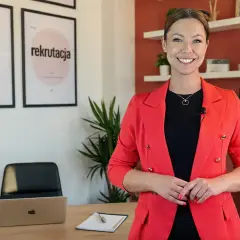 Uśmiechnięta kobieta w czerwonej marynarce, w tle plakaty "Kodeks pracy" i "Rekrutacja".