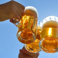 Trzy kufle złotego piwa wzniesione do toastu pod błękitnym niebem. Zastanawiasz się, ile węglowodanów ma piwo?