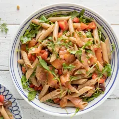 Pasta fredda con salmone affumicato, pomodorini, rucola e olive nere, guarnita con aneto fresco.