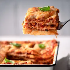 Ein Stück köstliche vegetarische Lasagne wird aus einer Auflaufform gehoben. Frisch, herzhaft und mit Basilikum garniert.