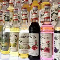 Rząd butelek syropów do kawy Monin o różnych smakach: od owocowych po kwiatowe, np. róża, lawenda, hibiskus.