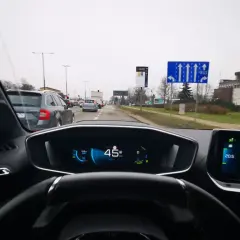 Znak drogowy informuje, kto może jeździć buspasem. Widok z wnętrza samochodu na drogę z innymi pojazdami.