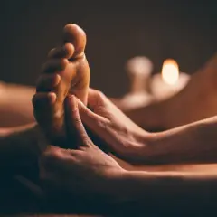 Mains expertes prodiguant un massage plantaire, révélant les bienfaits d'une détente profonde. Bougies tamisées en arrière-plan.