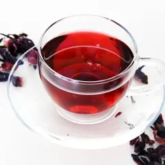 Szklana filiżanka z naparem z hibiskusa, otoczona suszonymi kwiatami. Czerwona herbata właściwości zdrowotne.