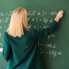 Nauczycielka pisze kredą wzory matematyczne na zielonej tablicy.