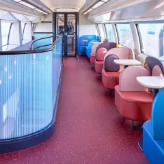 Wnętrze pociągu TGV inOui z kolorowymi siedzeniami i stolikami.