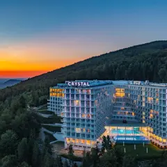 Nowoczesny hotel z widokiem na góry, oświetlony wieczorem, z basenem i tarasami.