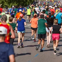 Tłum biegaczy pokonuje trasę. Czy wiedzieli, ile km ma maraton? Słońce i cień na asfalcie.