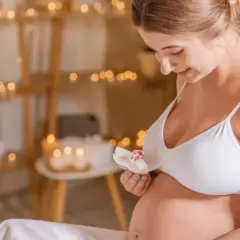 Uśmiechnięta ciężarna kobieta trzyma kwiat. Delikatne światła tworzą atmosferę relaksu, idealną dla kosmetyków dla kobiet w ciąży.