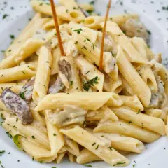 Penne w kremowym sosie z kawałkami mięsa i posypane natką pietruszki.