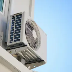 Unidad exterior de aire acondicionado montada en pared blanca, ideal para saber donde colocar la unidad exterior del aire acondicionado para una óptima ventilación.