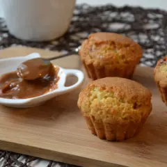 Trzy muffiny z toffifee na desce, obok sos karmelowy w białej miseczce.