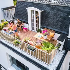 Ein Paar genießt ein Grillfest auf ihrem neu gestalteten Balkon. Der Balkon ist mit Holzmöbeln, Pflanzen und Dekorationen geschmückt.
