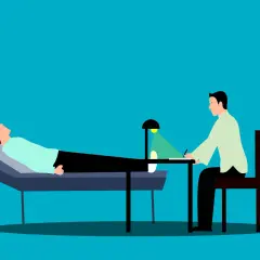 Pacjent leży na kozetce, a terapeuta prowadzi diagnozę psychologiczną, notując spostrzeżenia.