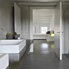 Salle de bain moderne avec murs en béton ciré, lavabos rectangulaires blancs et douche vitrée. La résine salle de bain offre un aspect brut et contemporain.