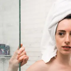 Ragazza con asciugamano in testa guarda preoccupata la doccia, pensando che la paraffina liquida fa male alla pelle.