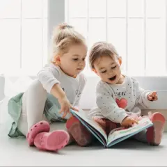 Dwie dziewczynki, jedna 1,5 roczne dziecko mówi tylko po swojemu, przeglądają kolorową książeczkę.