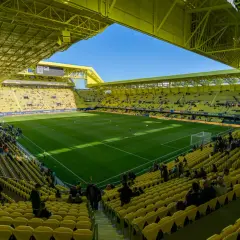 Stadion Villarreal, wypełniony żółtymi siedzeniami, z zieloną murawą i błękitnym niebem.