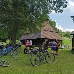 Grupa rowerzystów odpoczywa przy drewnianej cerkwi, planując dalszą podróż po malowniczych trasach rowerowych Bieszczad.
