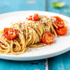 Spaghetti conditi con una cremosa salsa alle melanzane, guarniti con pomodorini confit e parmigiano grattugiato.
