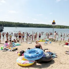 Tłum ludzi odpoczywa nad jeziorem w Wielkopolsce. Kąpielisko tętni życiem, w wodzie i na plaży widać wielu kąpiących się i plażowiczów.