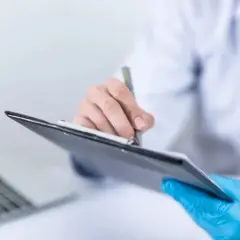 Lekarz w niebieskich rękawiczkach pisze na tablicy, obok laptop.