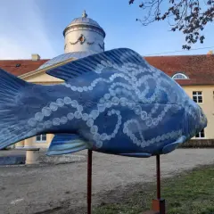Niebieska rzeźba ryby z perłami zdobi teren w Dolinie Baryczy, idealne miejsce na trasy spacerowe.