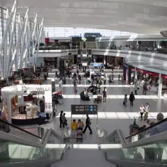 Tętniący życiem terminal lotniska w Budapeszcie. Pasażerowie przemieszczają się między sklepami i kawiarniami, a nowoczesna architektura tworzy przestronne wnętrze.