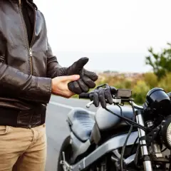 Hombre con chaqueta de cuero se pone guantes junto a una moto. ¿Listo para vender moto sin papeles?