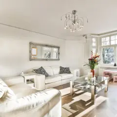 Jasny salon z białymi sofami, szklanym stolikiem i ozdobnym lustrem. Inspiracje salonem w stylu francuskim.