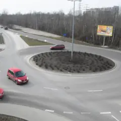 Samochody krążą po rondzie turbinowym. W tle drzewa i budynki.