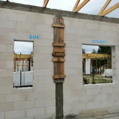 Budowa domu z bloczków betonowych, widoczne okna i drzwi z tymczasowym nadprożem, drewniane elementy konstrukcyjne.