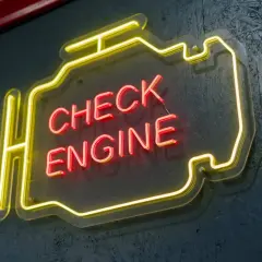 Neonowy napis "CHECK ENGINE" w kształcie silnika, świecący na czerwono i żółto, ostrzega przed awarią.