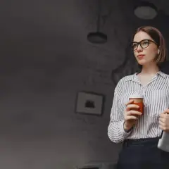 Kobieta w okularach trzymająca kawę i laptopa.