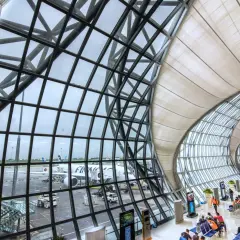 Moderne Architektur am Flughafen Bangkok: Flugzeuge stehen bereit, während Reisende im Wartebereich auf ihren Abflug warten.