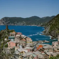 Colorful houses cling to the cliffs of the Cinque Terre Italy coast, overlooking a vibrant blue sea. A medieval tower stands guard.