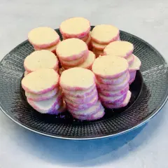 En hög med hembakade brysselkex med rosa sockerkanter ligger på en mörk tallrik. Perfekt för fikat!