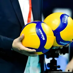 Dwie piłki do siatkówki Mikasa w rękach mężczyzny w garniturze. Czy wiesz, do ilu setów gra się w siatkówce?