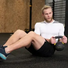 Mężczyzna wykonuje brzuszki z obciążeniem, trzymając kettlebell.