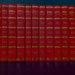 Eine Reihe roter Bücher mit goldener Verzierung, die Werke von Alexandre Dumas dem Älteren enthalten.
