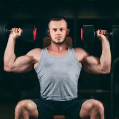 Mężczyzna wykonuje wyciskanie hantli nad głowę, jedno z najlepszych ćwiczeń na barki.