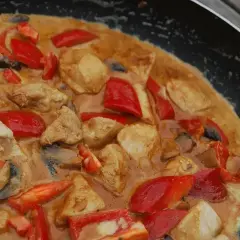 En krämig gryta med kyckling, champinjoner och röd paprika i en panna.