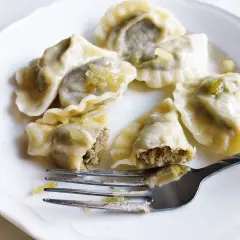 Pyszne pierogi z soczewicą na białym talerzu, jeden nadgryziony, obok widelec.